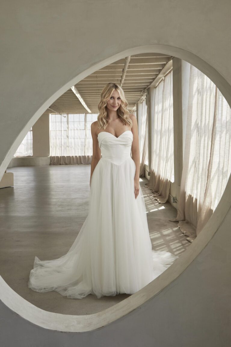 The May wedding dress epitomizes timeless elegance with a modern touch, ideal for the bride who values classic beauty and dramatic flair. Crafted from luxurious satin and ethereal tulle, the gown features a classic sweetheart neckline with intricate pleated detailing, adding depth and sophistication to the design. The bodice’s intense structure, highlighted by a curved bateau waistline, offers a flattering and refined silhouette. The full tulle skirt, with its heavy gathering at the waist, creates a voluminous, fairy-tale effect that enhances the gown’s romantic charm. Inspired by the grandeur of vintage ball gowns, the May dress is perfect for an opulent ballroom wedding or an elegant indoor ceremony, capturing the essence of graceful sophistication and timeless beauty.