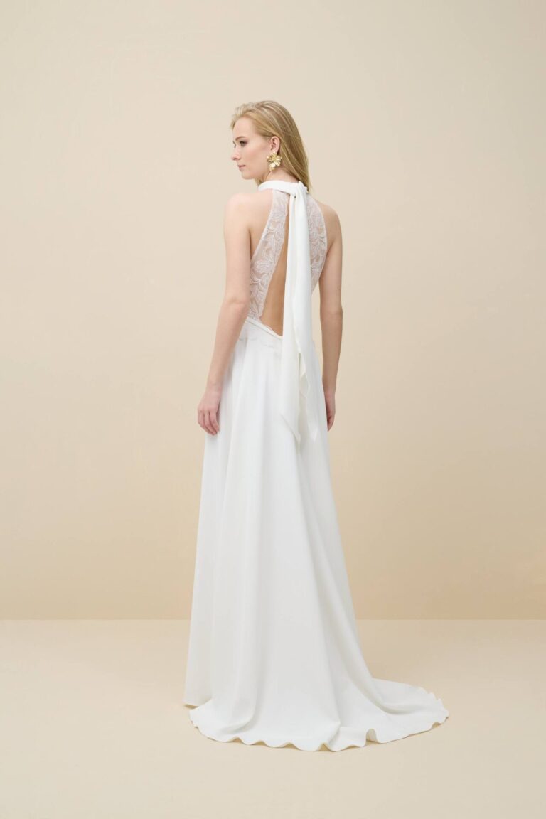 Promesse is a modern and romantic wedding dress. The top features a halter neckline of ivory lace that touches the skirt. A detachable crepe scarf completes the look. The crepe skirt has an A-line fit and a train.